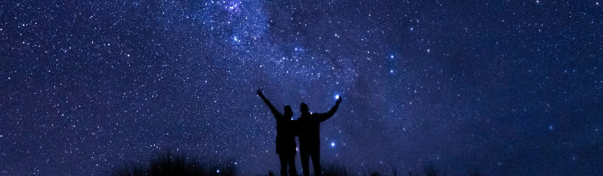 Paar auf Hügel vor nächtlichem Sternenhimmel